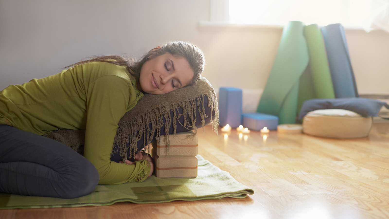 Woman relaxing and restoring on a yoga mat with restorative yoga props