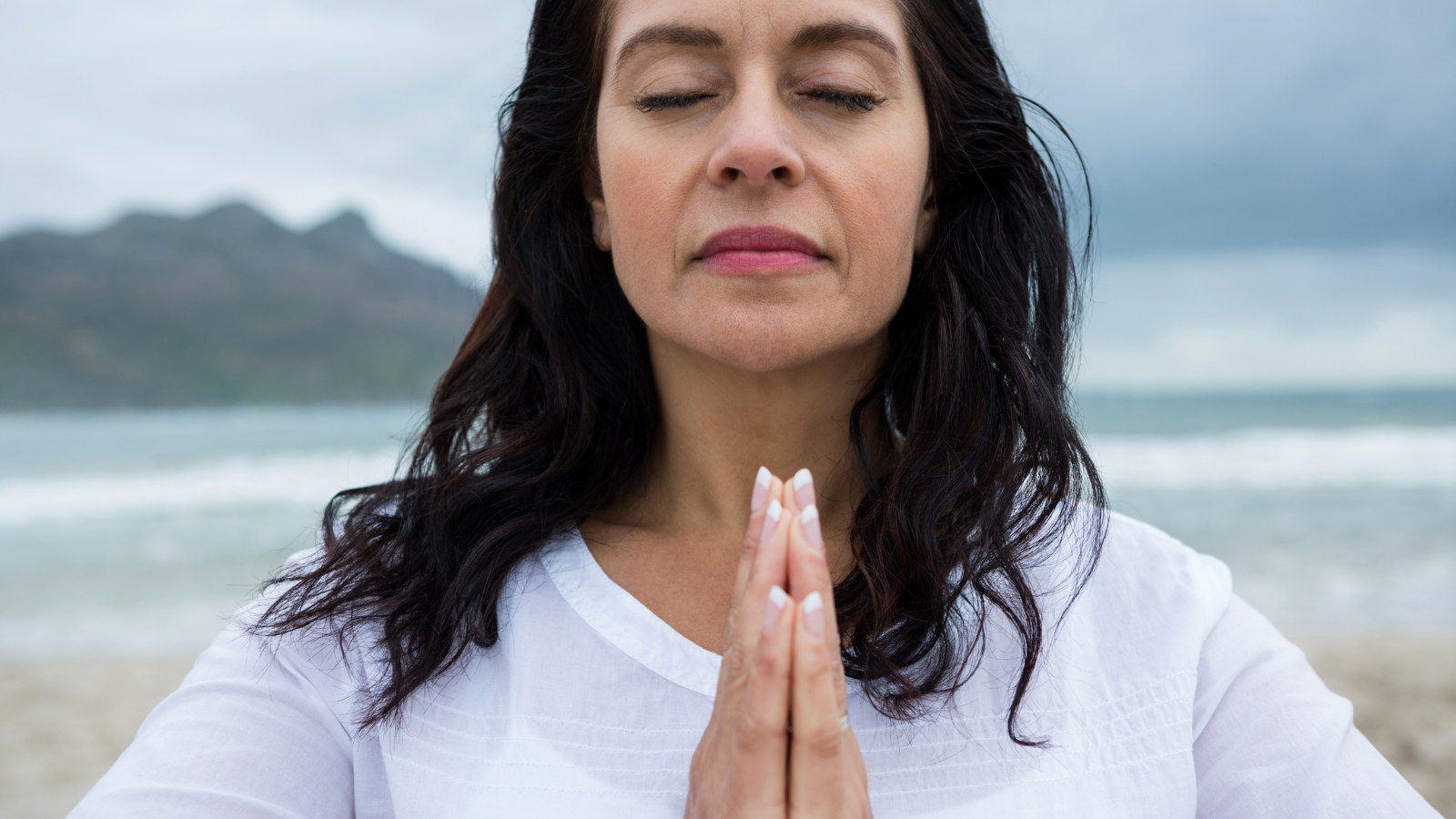 Woman in contemplative state with hands in Anjali Mudra representative of opening the heart chakra