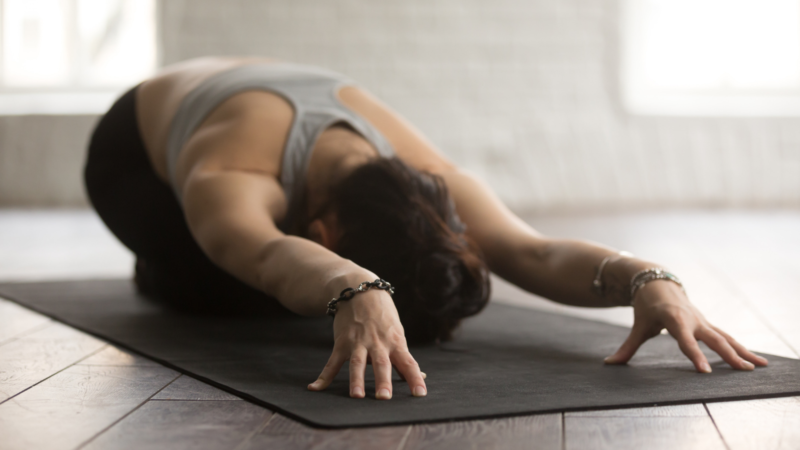 Young beautiful sporty yogi woman practicing yoga concept, sitting in Child exercise on black yogic mat, Balasana pose, working out, wearing sportswear