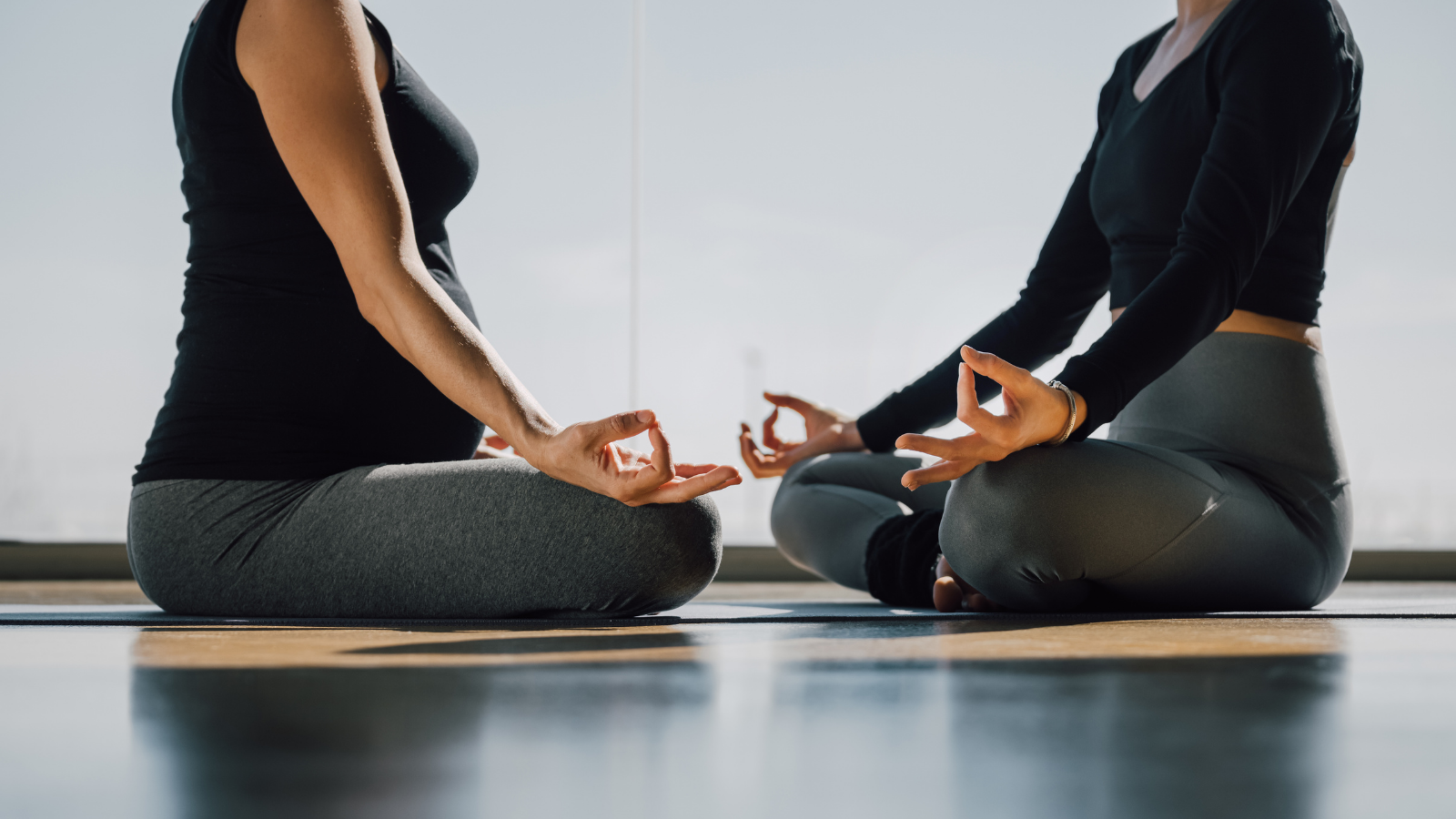 Close up of two woman sitting cross-legged in Padmasana, Lotus posture, yoga hands pose, fingers in Jnana mudra