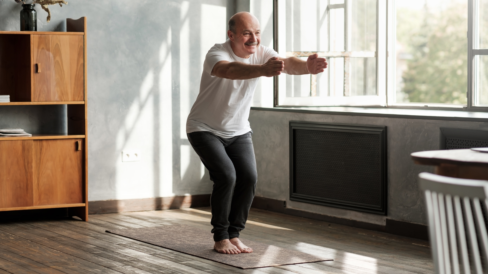 Senior hispanic man practicing yoga indoors at living room doing Chair pose or Utkatasana