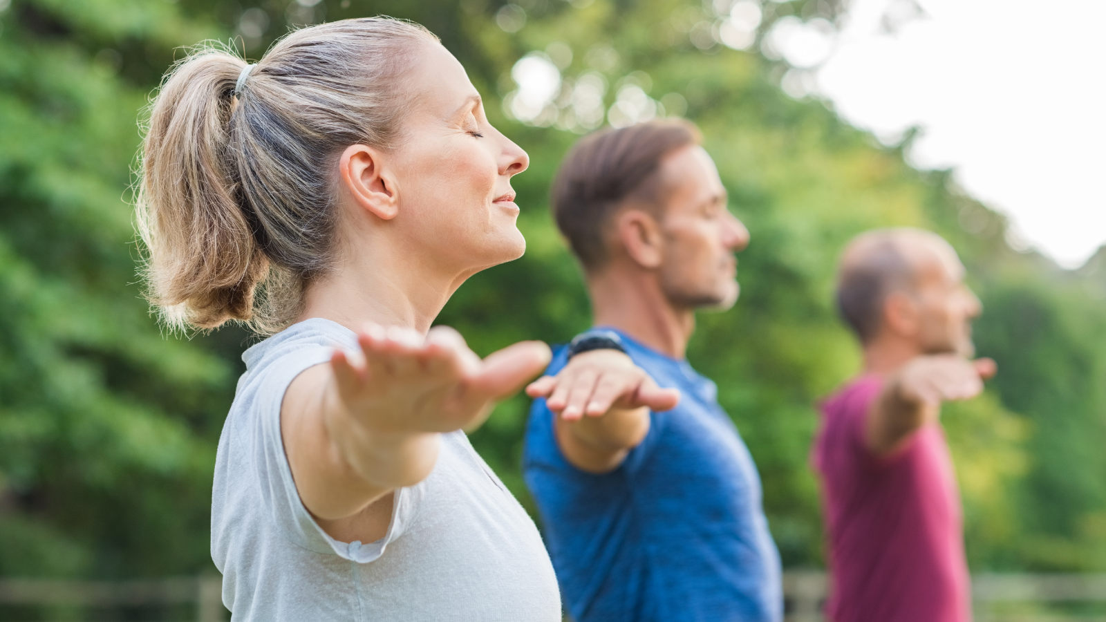 Group of senior people with closed eyes stretching arms at park