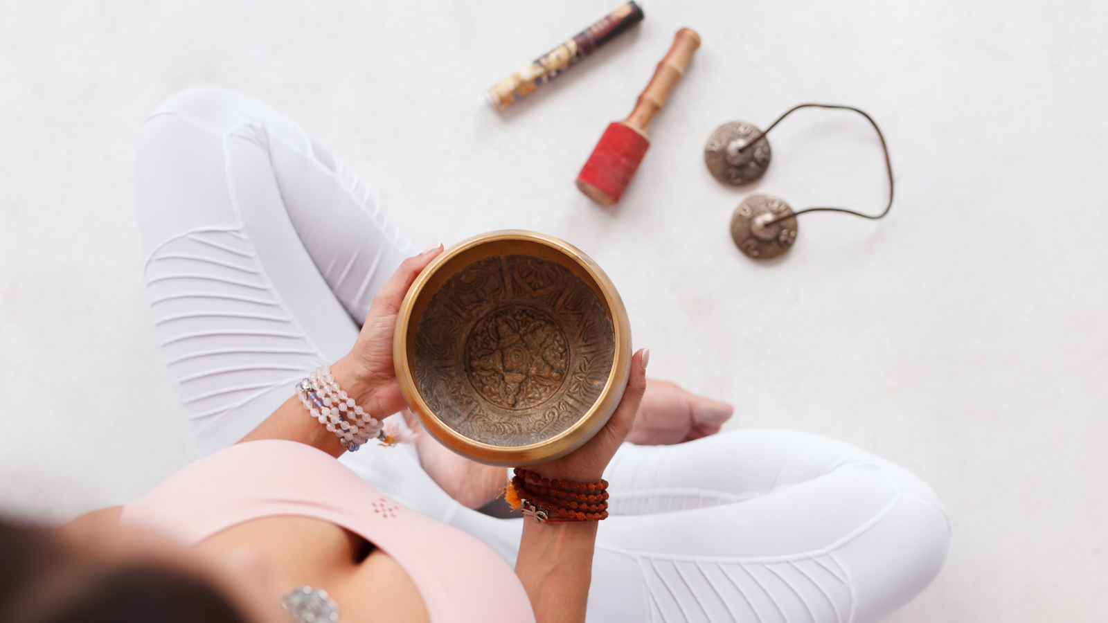 Young woman holding Tibetan singing bowl and pestle sitting on the floor next to mortar and fragrant candles for yoga and meditation and just breathe