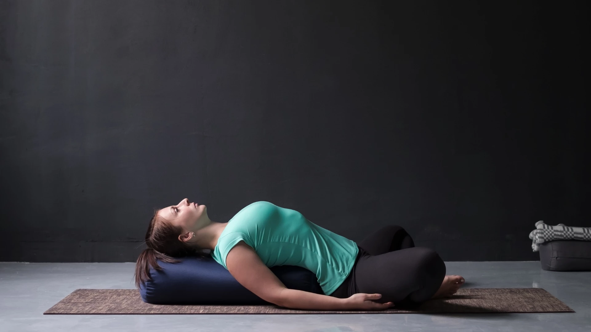 Young attractive woman practicing yoga concept, lying in Reclined Butterfly exercise, supta baddha konasana pose. Full length view