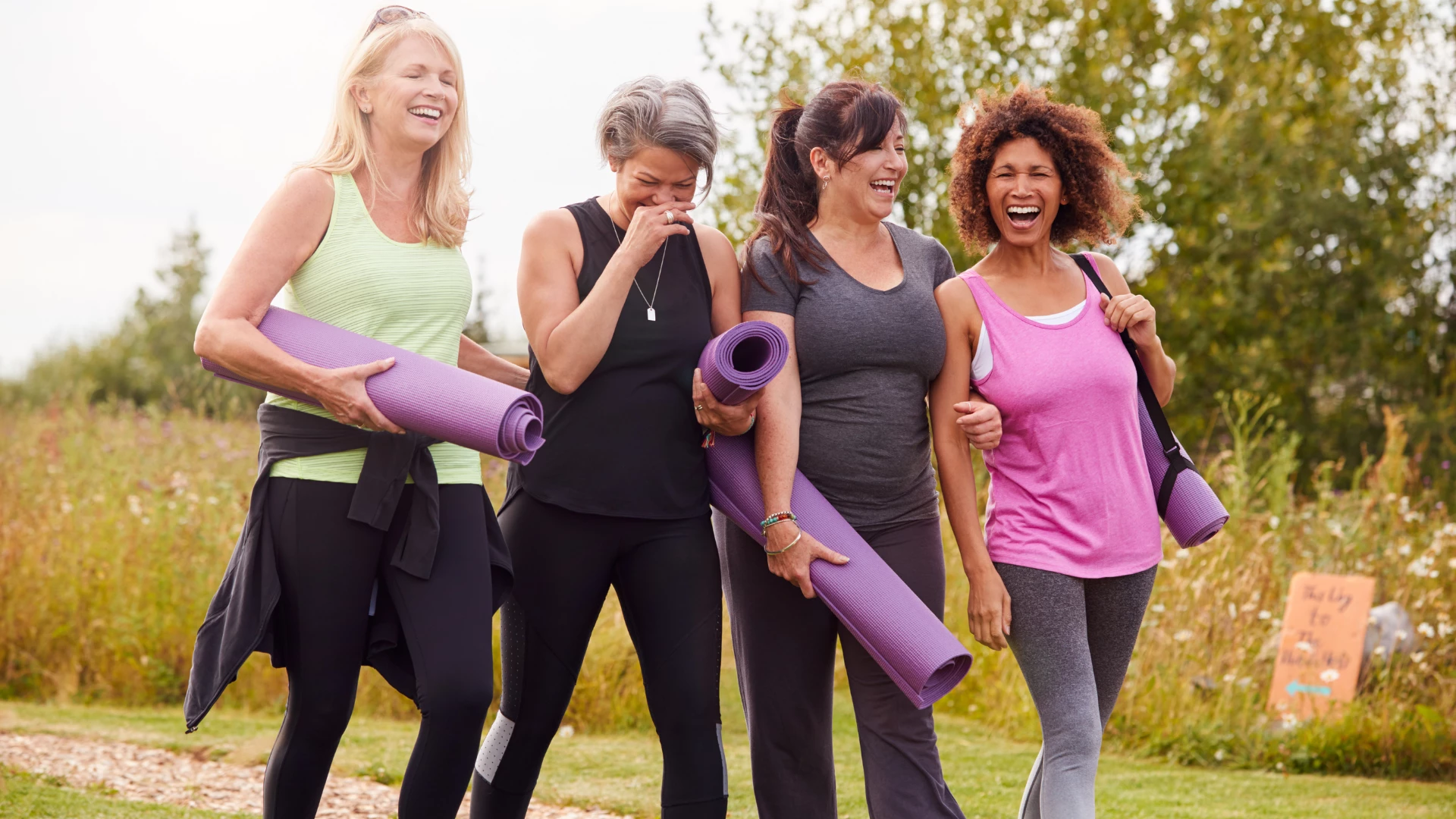 Group Of Mature Female Friends On Outdoor Yoga Retreat Walking Along Path Through Campsite