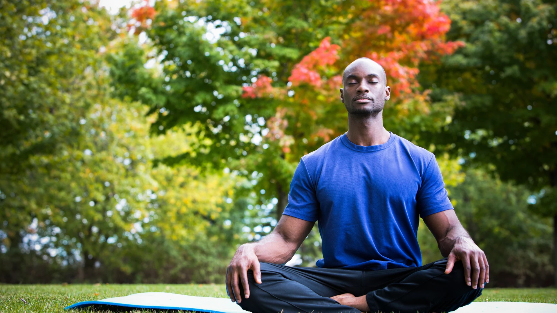 Young black man wearing athletic wear sitting in the park meditating - being in nature and meditating are both critical steps to healthy vibrant aging.