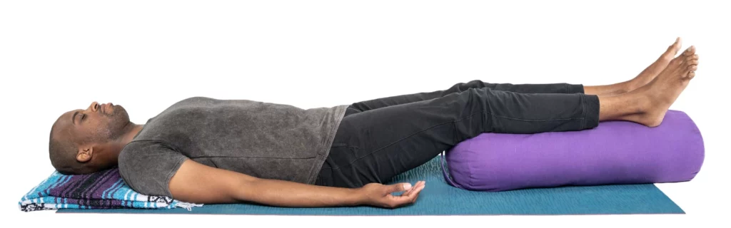 Beginner yoga student enjoys the benefits of a Corpse Pose modification for back pain (Sanskrit name: Savasana)