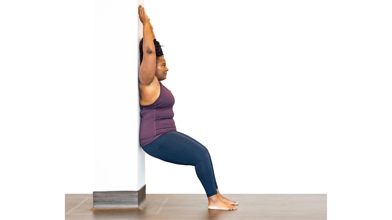 Yoga student demonstrates how to do a modification of Chair Pose at the wall (Sanskrit name: Utkatasana)