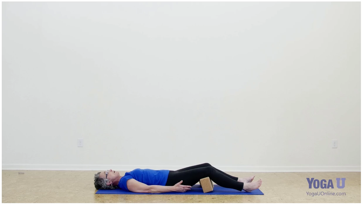 Corpse Pose or Savasana with the support of a block under the knees after exploring the glutes' role in backbends