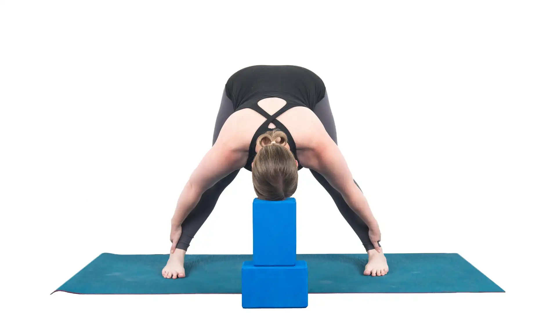 Woman practicing wide-leg forward bend with support under her head.