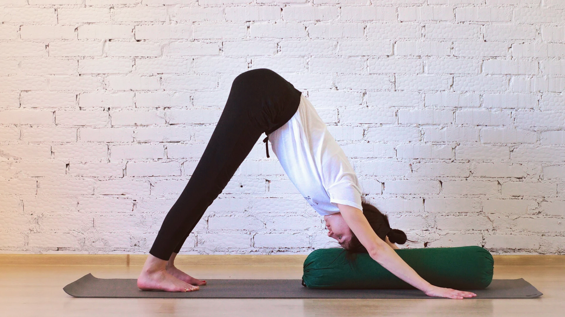 Woman practicing yoga downward facing dog with bolster under her head for support.