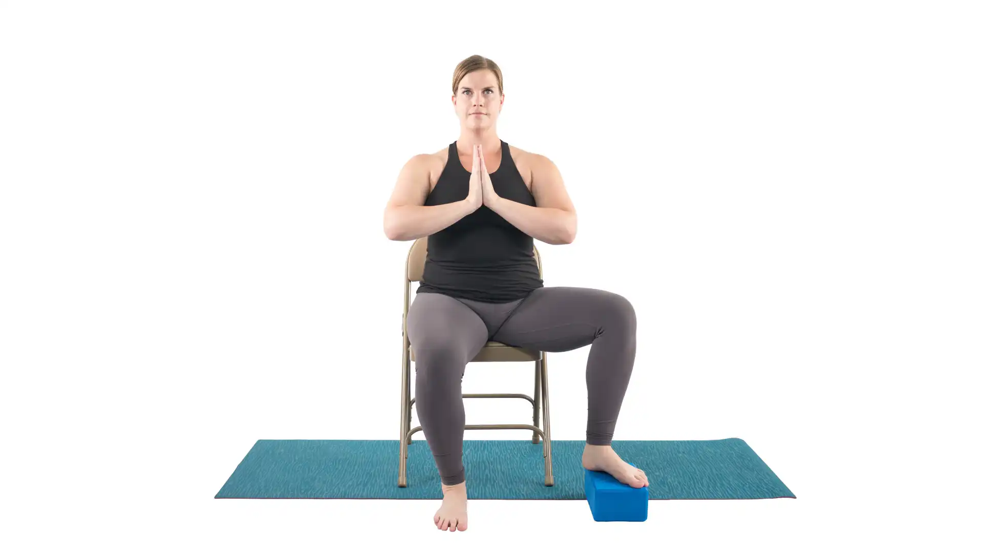 Woman practicing accessible version of tree pose seated in a chair with a block for her foot.