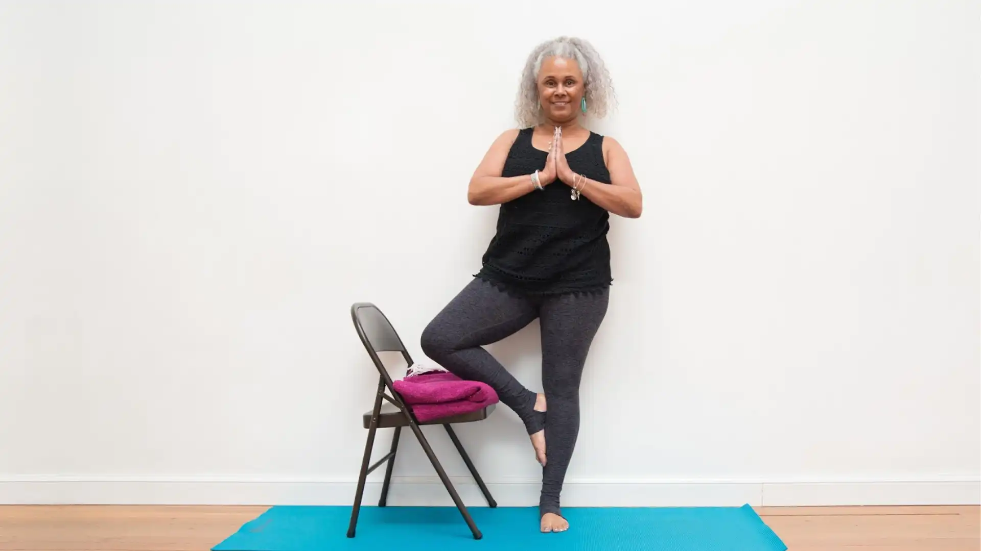 Woman practicing yoga tree pose with chair.