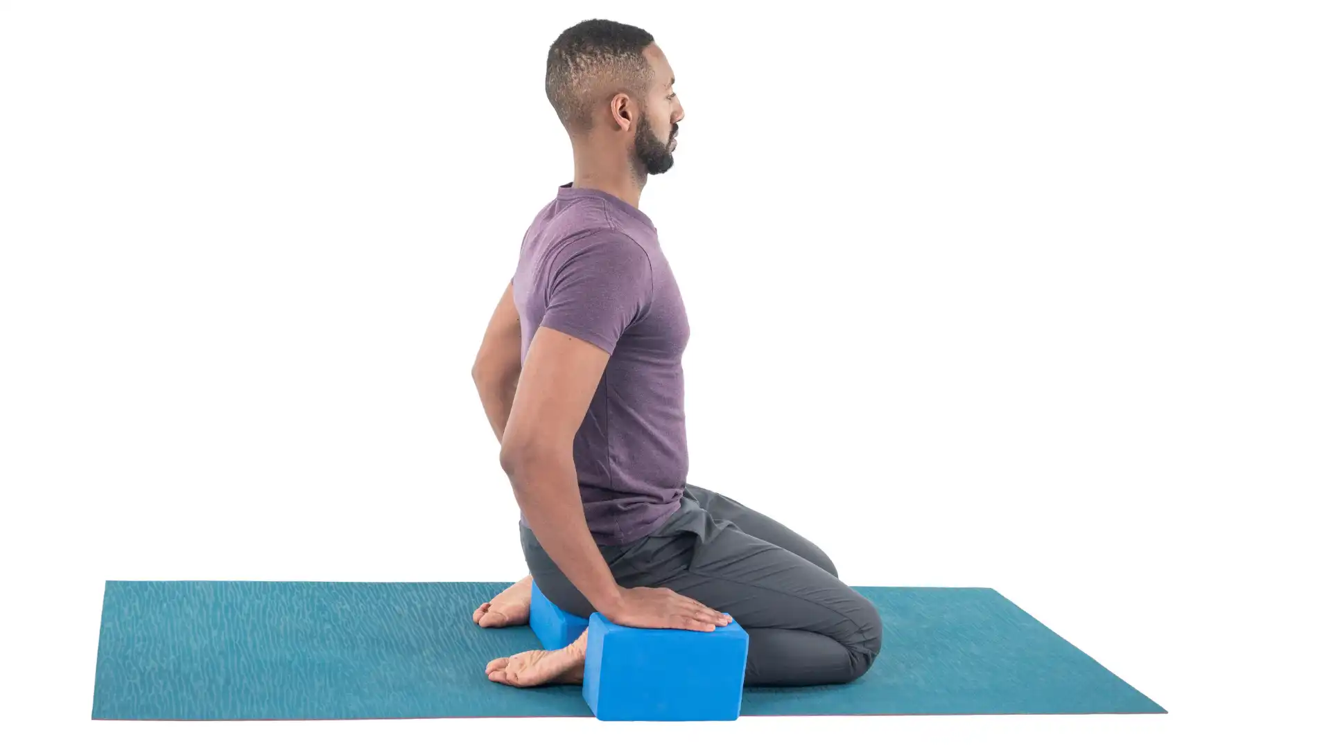 Man practicing virasana, hero pose, yoga with blocks.