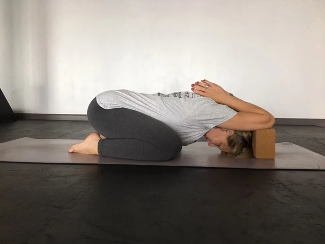 woman practicing yoga, in modified child's pose (balasana) using blocks to open shoulders