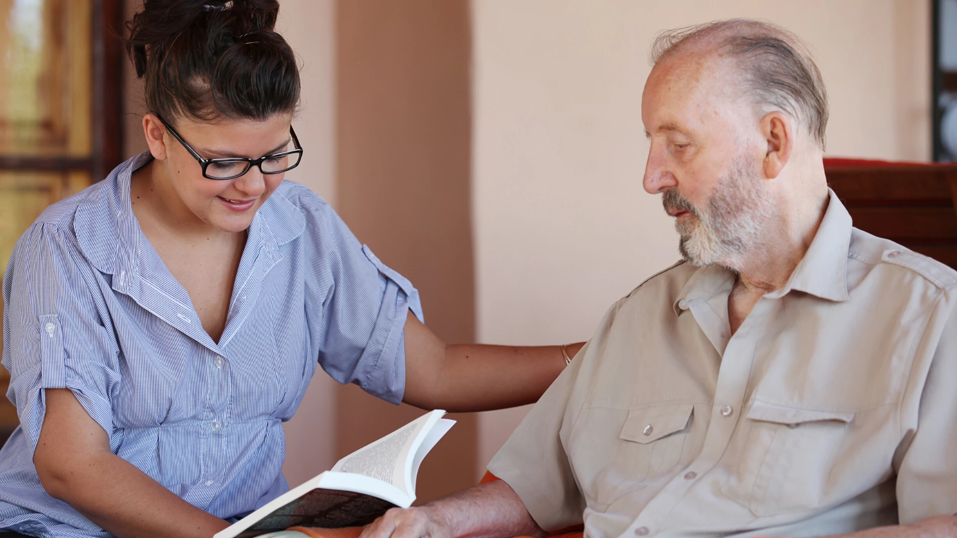 Woman practicing yoga seva reading to older man.