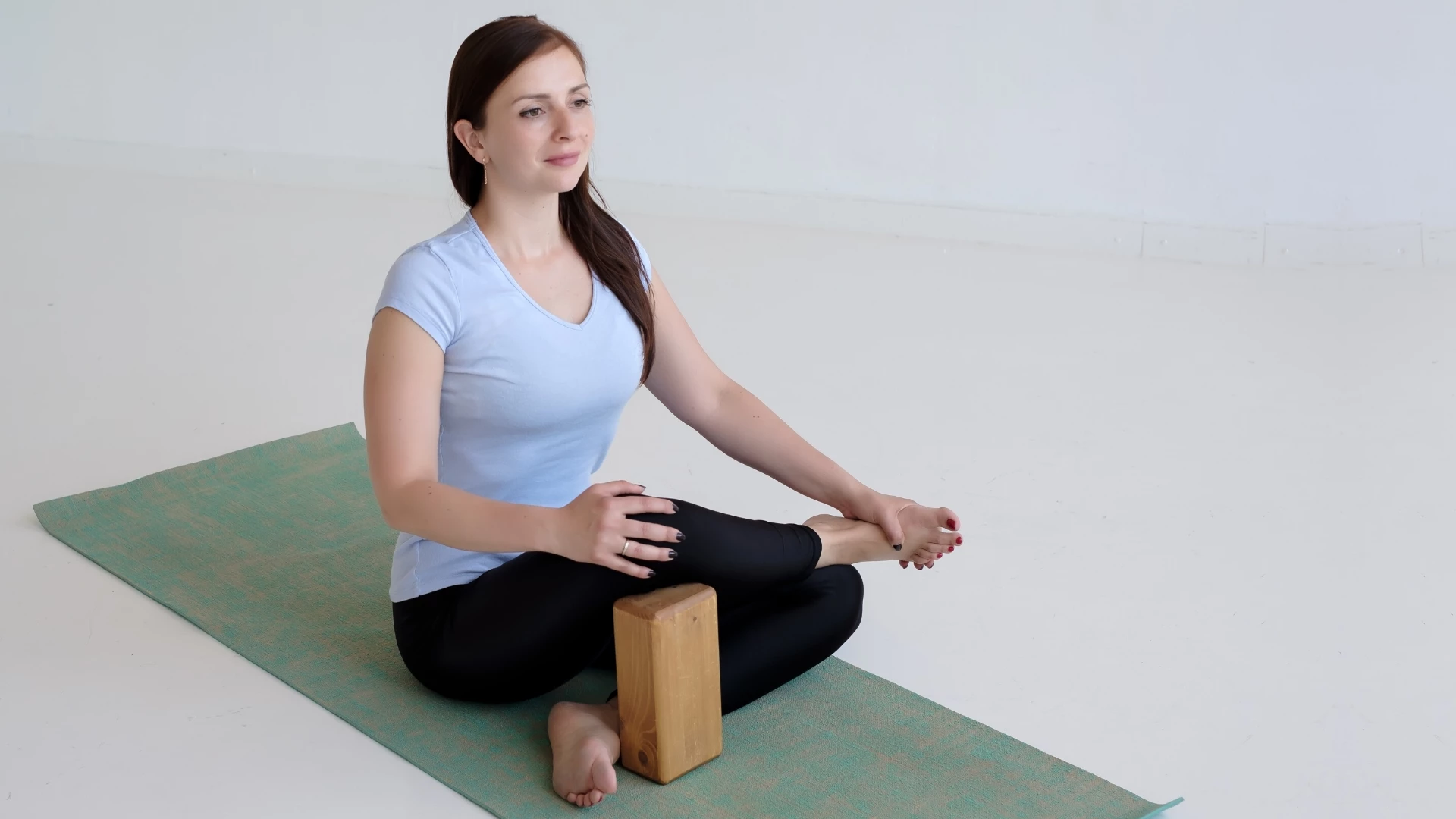 Woman practicing seated pose with yoga block for support.