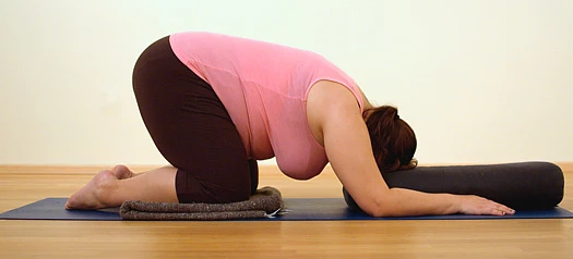 woman in safe child's pose yoga modification using mat under knees and bolster under forehead