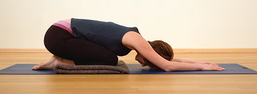 Woman in child's pose yoga modification using mat under knees