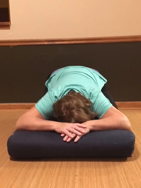 Woman in Child's Pose (Balasana) to reduce neck and head tension with a pillow, practicing restorative yoga