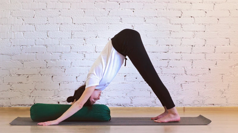 Woman practicing Downward Facing Dog with a bolster under her head