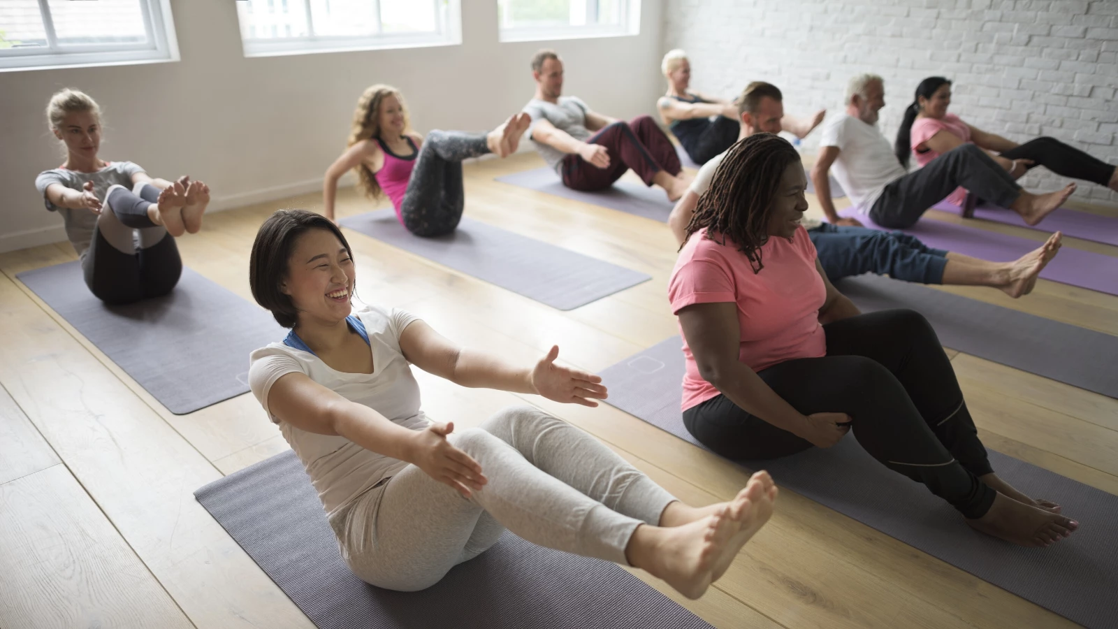 Group of diverse yoga students practicing boat pose.