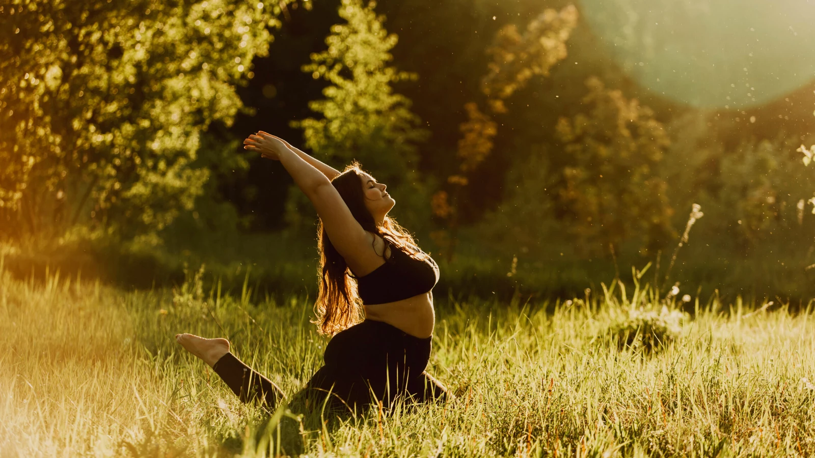 Curvy woman practicing pigeon pose in the grass.