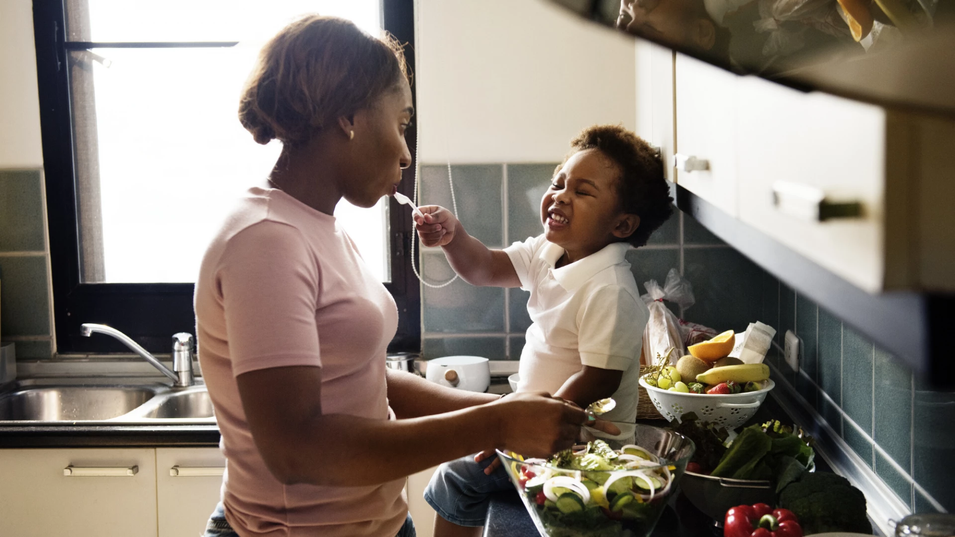 Little boy feeding his mother food while cooking.