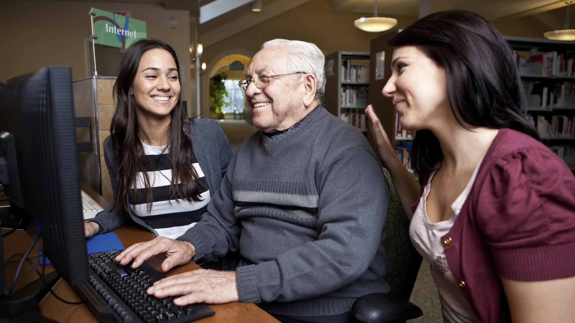 Two girls helping elderly man on the computer.