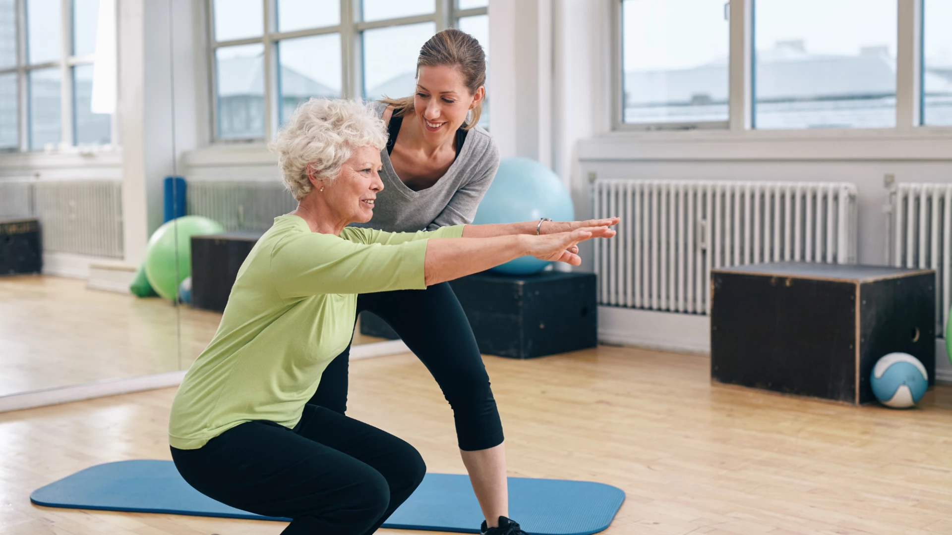 Older woman being coached in yoga chair pose.