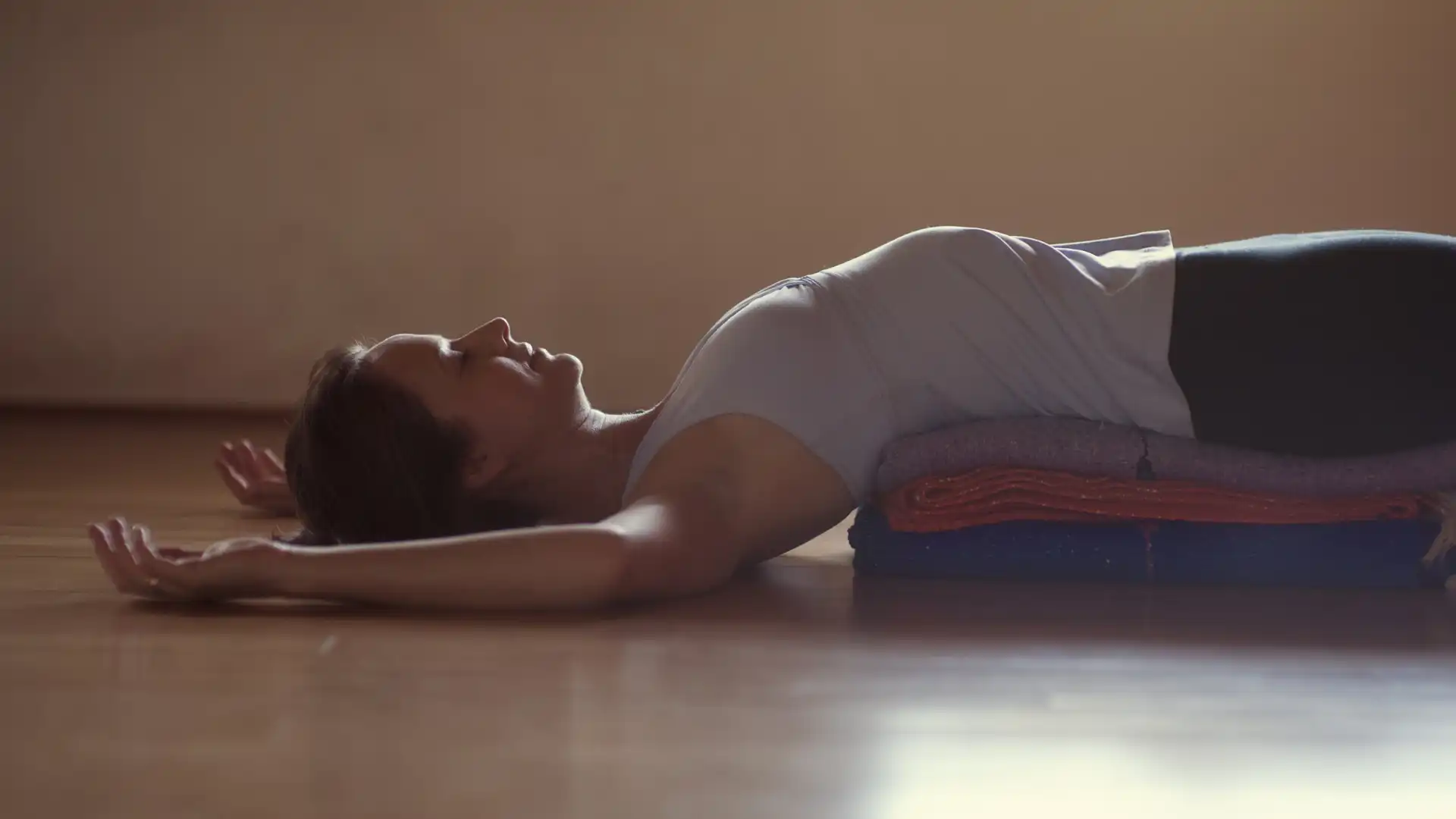 side view of woman practicing supported back bend with blankets under her.