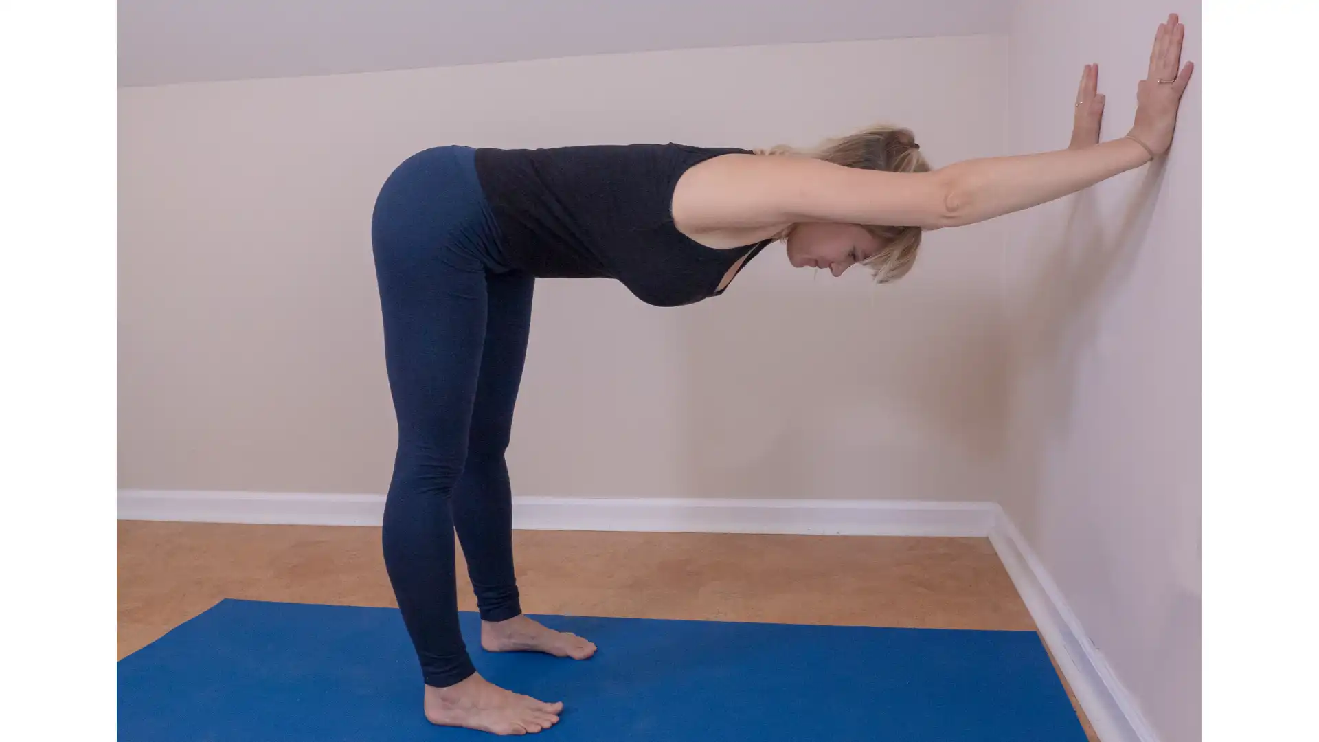 Woman practicing yoga downward dog pose (Adho Mukha Svanasana) at the wall.