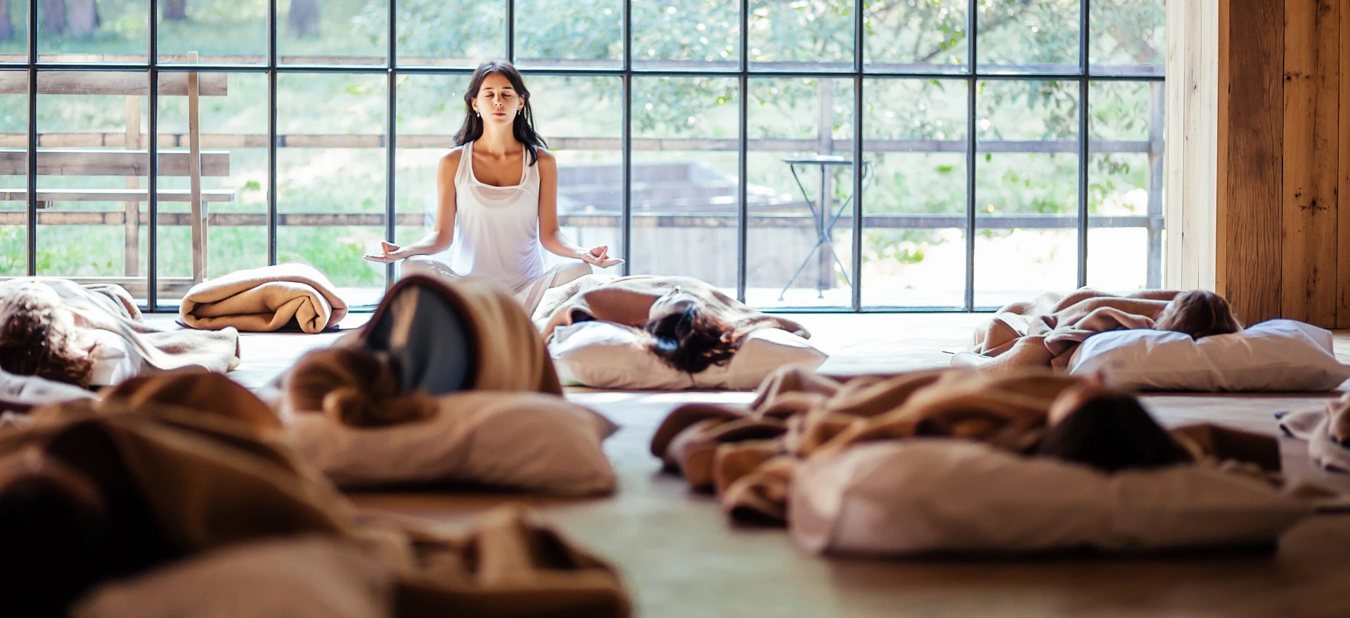 Yoga instructor meditates during her yoga class while students rest in savasana.