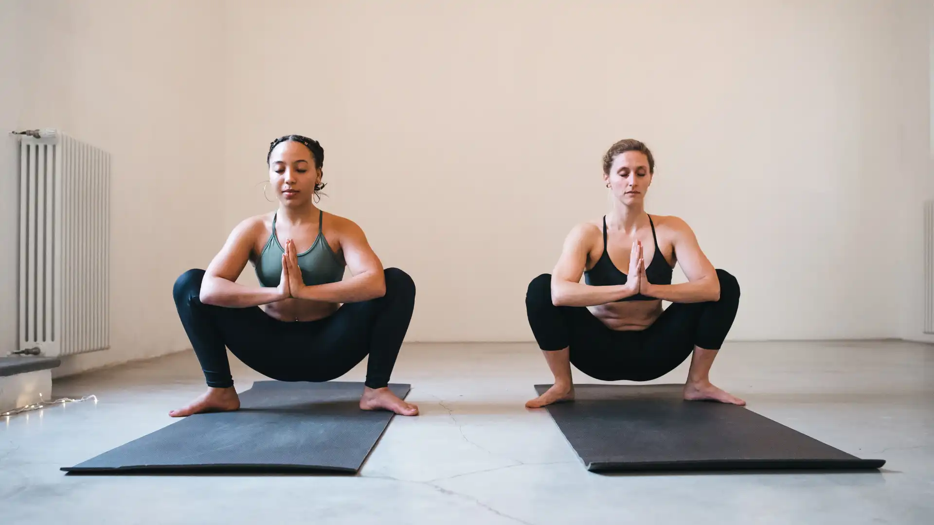 Two yoga students practicing malasana - yogic squat in yoga class.