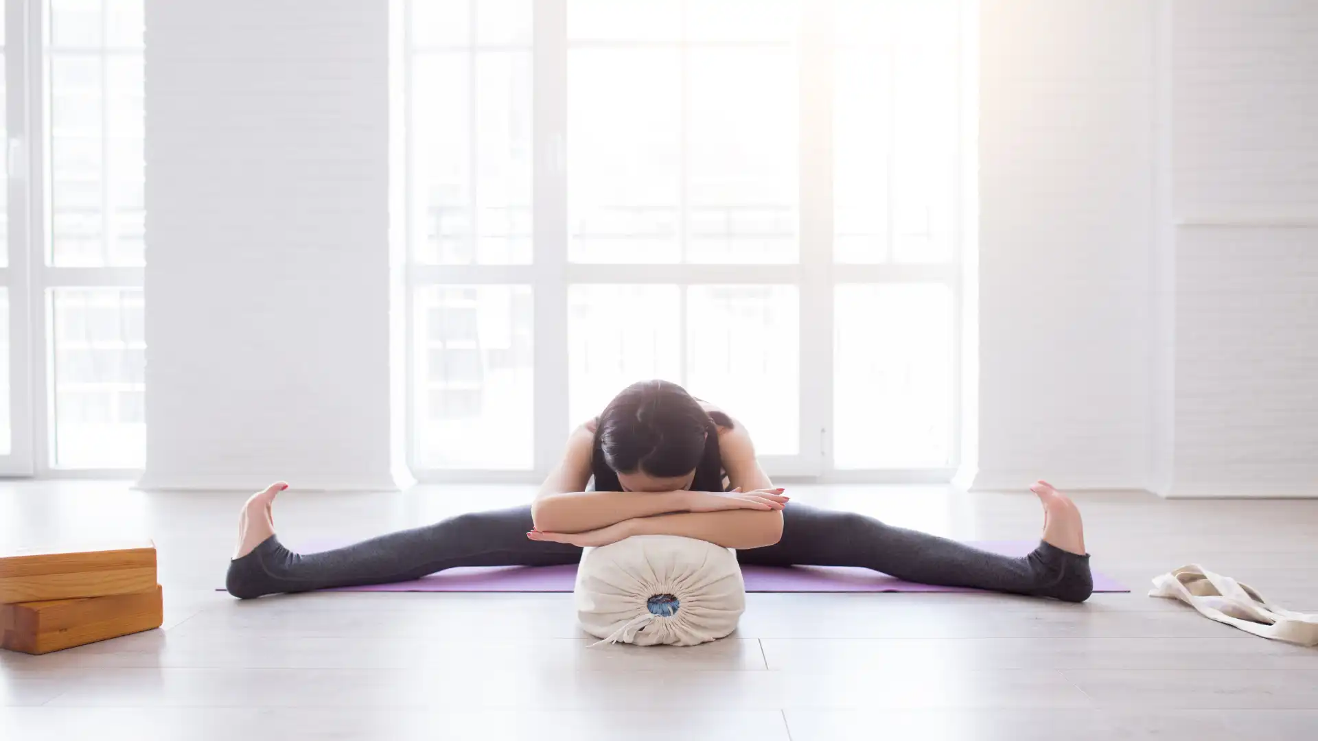 Woman practicing yoga supported wide leg forward bend.