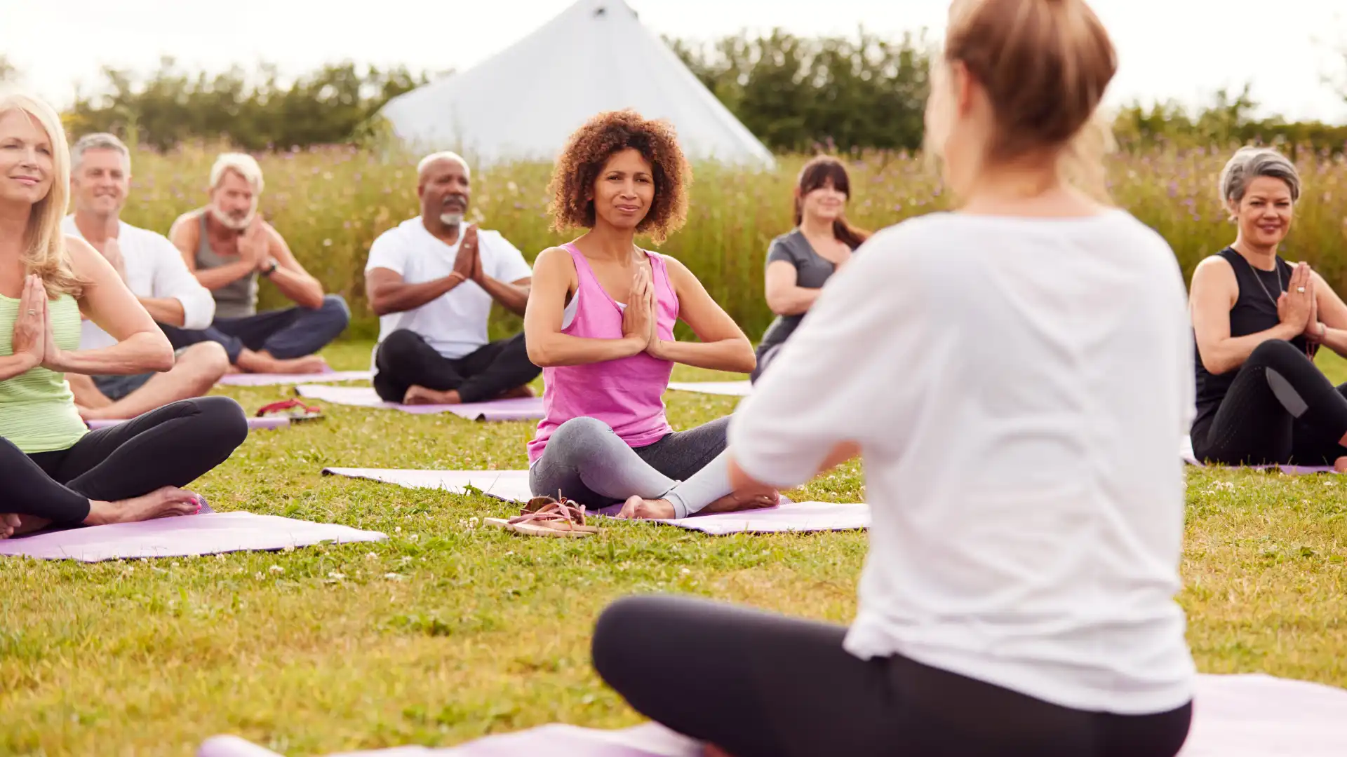 group of middle-aged yoga students practicing yoga outdoors.