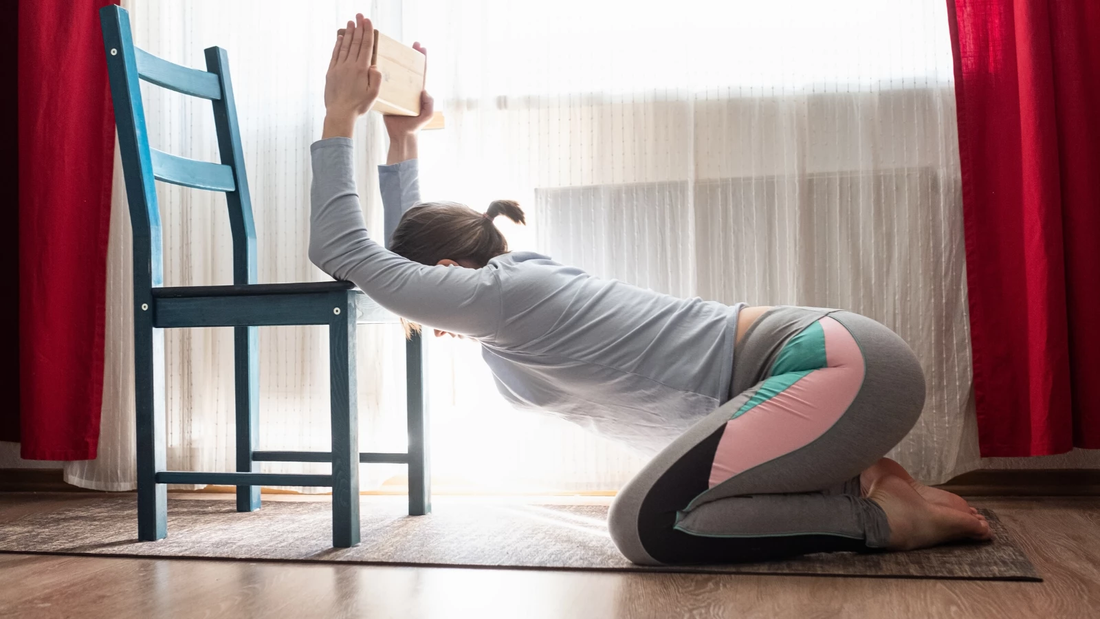 female yoga student practicing gentle yoga with a chair at home.