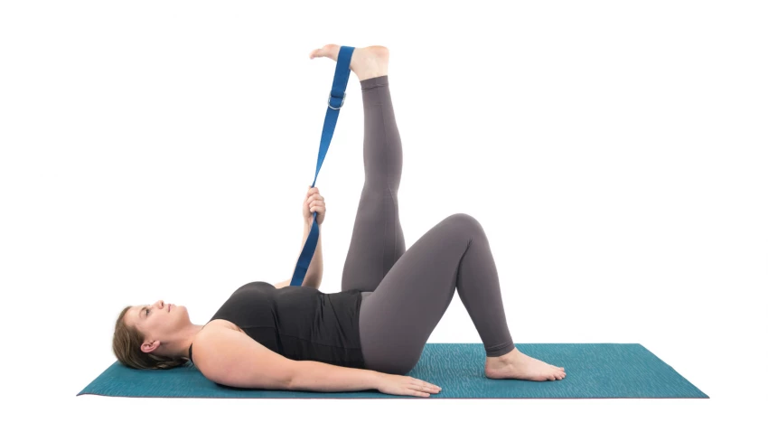 Yoga student practicing the supine pose Supta Hasta Padangusthasana with the help of a yoga strap