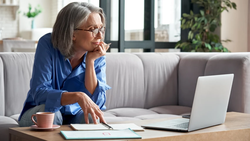 older woman taking online webinar on laptop remote working or social distance learning from home