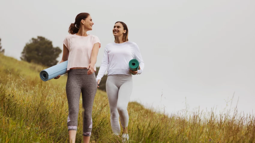 Smiling friends in fitness wear walking in the meadows with yoga mats