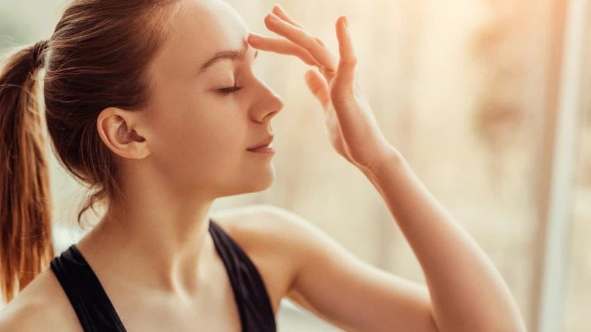 Side view of beautiful young female with closed eyes touching Ajna chakra on her forehead