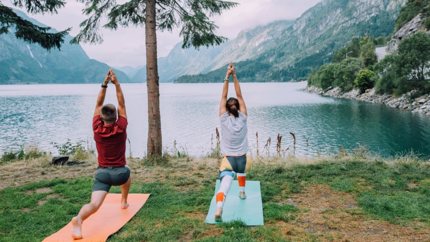 Fitness lifestyle concept - sportive couple making yoga exercises sitting on mats outdoors near lake