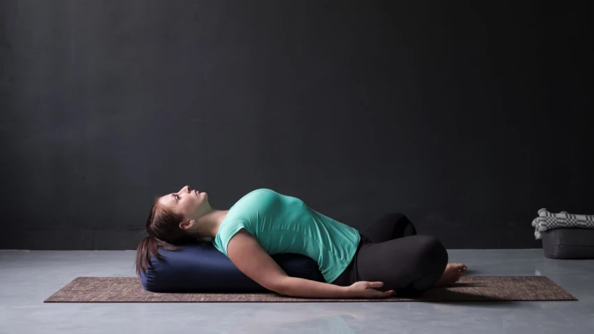 woman practicing yoga lying in Reclined Butterfly pose (Supta Baddha Konasana), heart opening pose