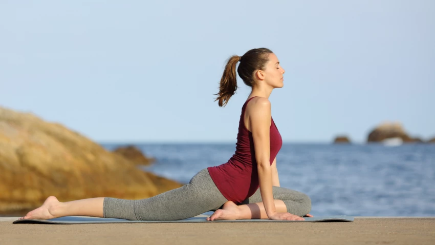 Woman doing Urdhva Mukha Svanasana (Upward Facing Dog) during travel to the beach