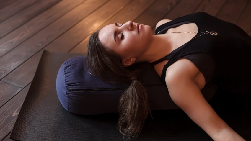 Woman resting after a yoga class in Corpse Pose or Savasana with bolster for spine comfort