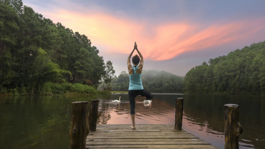 woman practicing yoga at lake surrounded by water, earth and sky representing ayurvedic elements