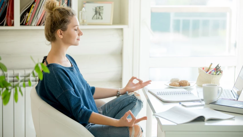 attractive woman in a chair seating in Lotus pose in front of table with laptop