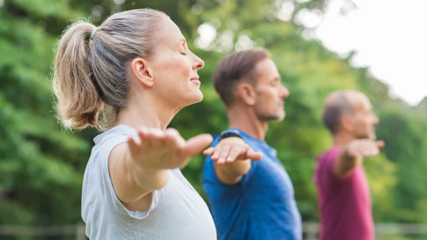 Group of senior people with closed eyes stretching arms at park. Happy mature people doing yoga