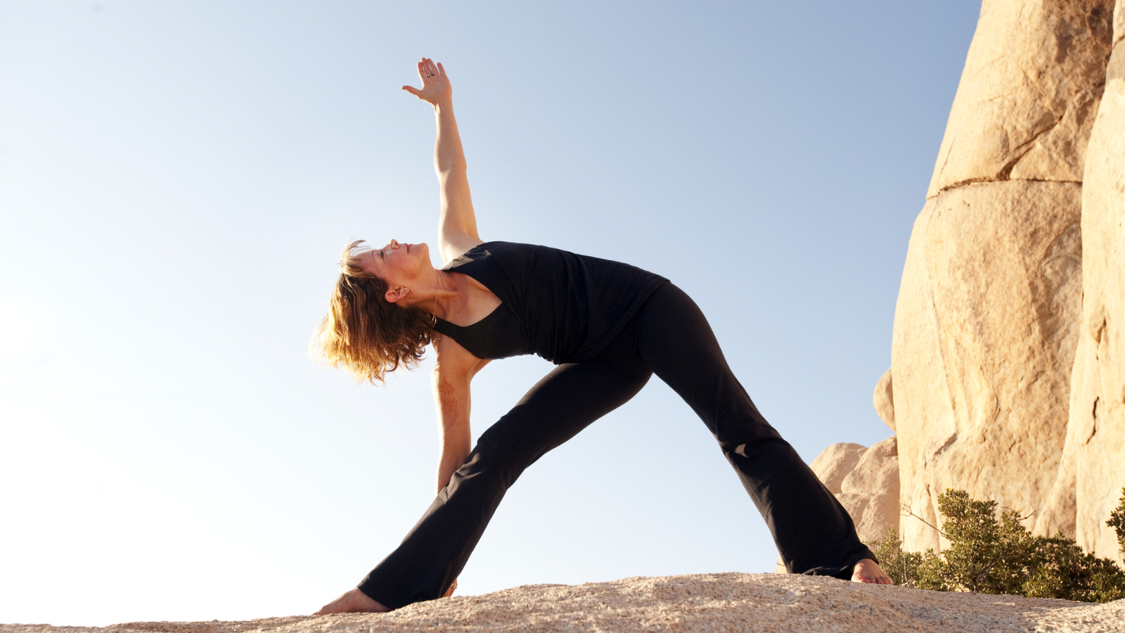 Woman, in Trikonasana or Triangle Pose in a natural boulder landscape. 