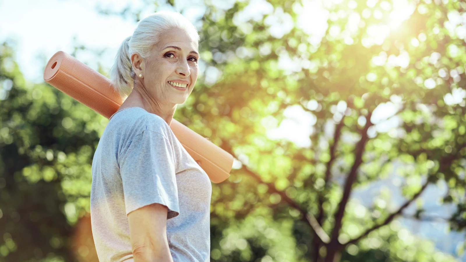 Lovely smiling mature woman looking calm while carrying her yoga mat